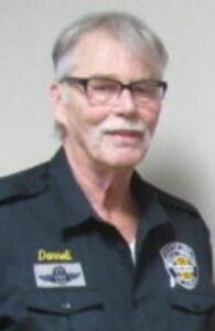 A man in police uniform with glasses and white hair.